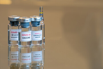 A close up set of three COVID-19 vaccination drug dose trial vials with a test ampule in the rear - 002