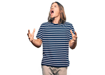Fototapeta na wymiar Handsome caucasian man with long hair wearing casual striped t-shirt crazy and mad shouting and yelling with aggressive expression and arms raised. frustration concept.