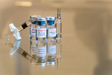 A set of three COVID-19 vaccination drug dose trial vials with a filled injection syringe in the front with a tiny droplet escaping from the needle tip with copy space - 028