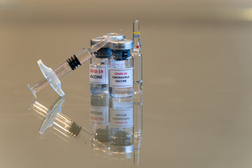 A set of COVID-19 vaccination drug dose trial vials with a filled injection syringe in the front with a tiny droplet escaping from the needle tip with copy space - 038