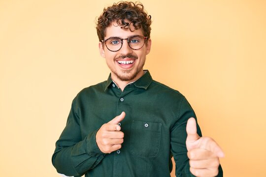 Young caucasian man with curly hair wearing casual clothes and glasses pointing fingers to camera with happy and funny face. good energy and vibes.