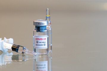 A closeup vial of COVID-19 Coronvavirus live virus biohazard culture with a syringe on the left and needle tip in the front - 089