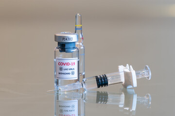 A closeup vial of COVID-19 Coronvavirus live virus biohazard culture with a syringe on the right and needle tip in the front - 091