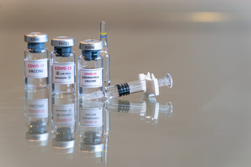 A closeup triple set of vials of COVID-19 Coronvavirus vaccine with a syringe on the right and needle tip in the front - 107
