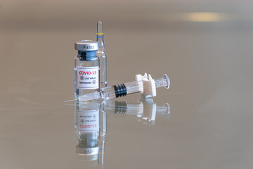 A closeup vial of COVID-19 Coronvavirus live virus biohazard culture with a syringe on the right and needle tip in the front - 120