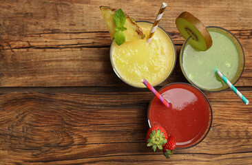 Delicious colorful juices in glasses on wooden table, flat lay. Space for text