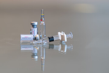 A sideways mini vial of COVID-19 Coronvavirus vaccine with a syringe on the right and an ampule a single mini vial in the rear - 132