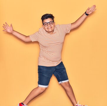 Adorable kid wearing casual clothes and glasses smiling happy. Jumping with smile on face and arms opened over isolated yellow background