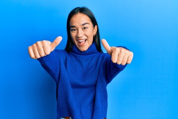 Young asian woman wearing casual winter sweater approving doing positive gesture with hand, thumbs up smiling and happy for success. winner gesture.
