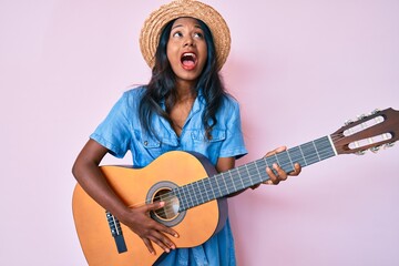 Young indian girl playing classical guitar angry and mad screaming frustrated and furious, shouting with anger looking up.