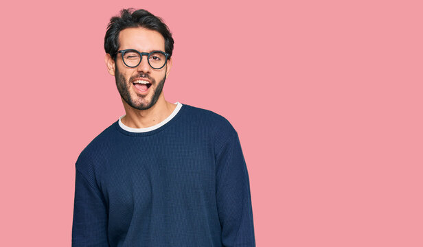 Young hispanic man wearing casual clothes and glasses winking looking at the camera with sexy expression, cheerful and happy face.