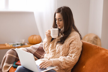 Beautiful young woman with laptop and cup of tea at home