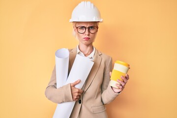 Young blonde woman with tattoo holding paper blueprints drinking take away cup of coffee skeptic and nervous, frowning upset because of problem. negative person.