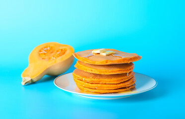 Plate with tasty pumpkin pancakes on color background