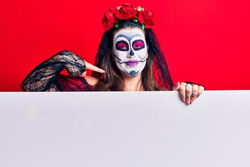 Young woman wearing day of the dead costume holding blank empty banner pointing finger to one self smiling happy and proud