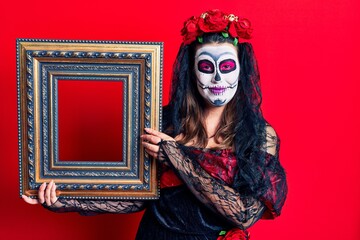 Young woman wearing day of the dead costume holding empty frame looking positive and happy standing and smiling with a confident smile showing teeth