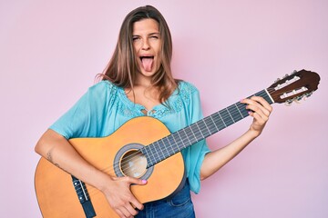 Beautiful caucasian woman playing classical guitar sticking tongue out happy with funny expression.