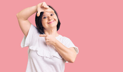 Brunette woman with down syndrome wearing casual white tshirt smiling making frame with hands and fingers with happy face. creativity and photography concept.