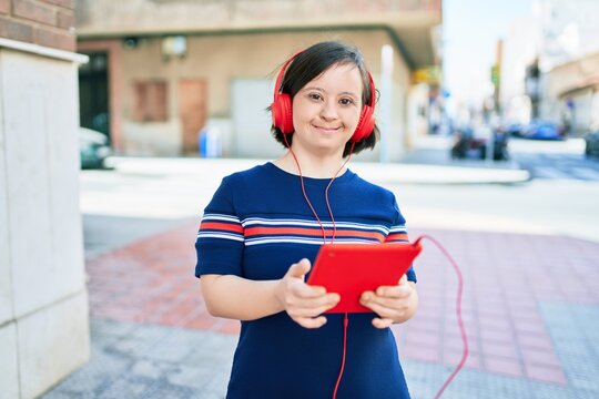 Beautiful Brunette Woman With Down Syndrome At The Town On A Sunny Day Using Touchpad Device Listening To Music Wearing Headphones