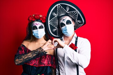 Couple wearing day of the dead costume wearing medical mask smiling in love showing heart symbol and shape with hands. romantic concept.