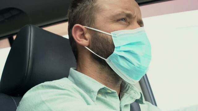 Adult man driving car wearing protective face mask during the coronavirus epidemic. Businessman in a medical mask is driving a car. Traveling by car during a pandemic COVID-19 coronavirus infection.