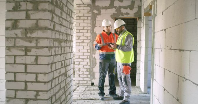 Contractors discussing construction data on tablet in corridor