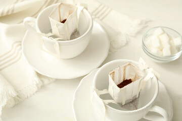 Cups with drip coffee bags on white table, closeup
