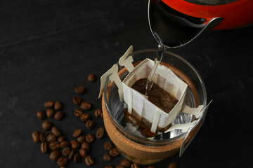 Fototapeta na wymiar Pouring hot water into cup with drip coffee bag on black table, closeup