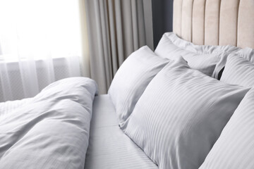 Comfortable bed with soft blanket and pillows indoors, closeup