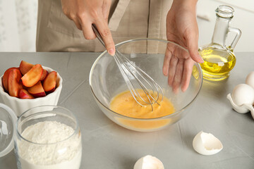 Woman whipping eggs at grey table, closeup. Cooking of delicious cake