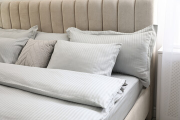Many soft pillows and blanket on large comfortable bed indoors