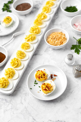 Two Deviled Eggs on a White Plate with a Deviled Egg Bar behind on a Marble Countertop