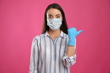 Woman in protective face mask and medical gloves pointing at something on pink background