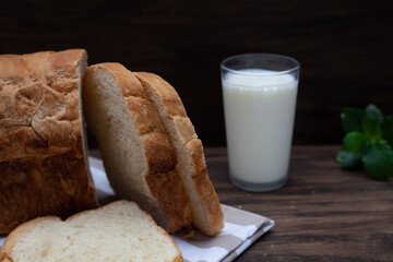 Homemade bread in focus ahead with glass of milk and slightly blurred green leaves in the background. Wood background.