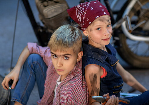 Children Sit Near With Motorcycle. Girl In A Red Bandana And Blue Overalls. Children Sit Back To Back