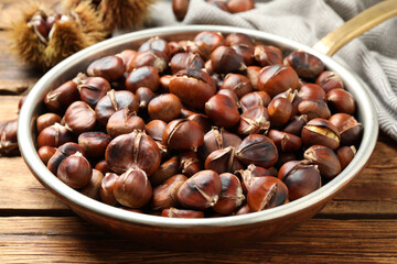 Delicious roasted edible chestnuts in frying pan on wooden table, closeup
