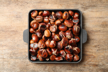 Delicious roasted edible chestnuts in baking dish on wooden table, top view