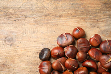 Delicious roasted edible chestnuts on wooden table, flat lay. Space for text