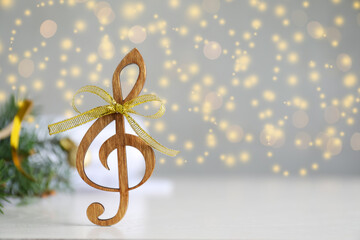 Wooden music note with golden bow on light grey table against blurred Christmas lights. Space for...