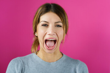 Young adult caucasian woman doing face yoga gymnastics for non-surgical rejuvenation and self-care mouth open with pink background - anti aging concept