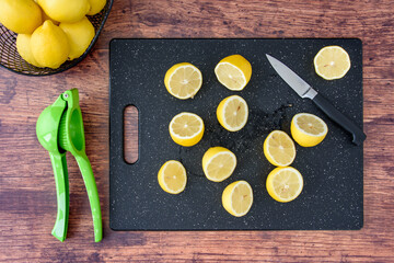 Fresh lemon halves on a black cutting board, paring knife, wood table, basket of lemons, citrus...