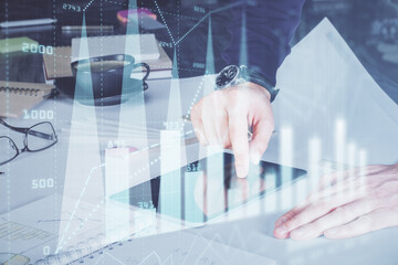 Double exposure of man's hands holding and using a digital device and forex graph drawing....