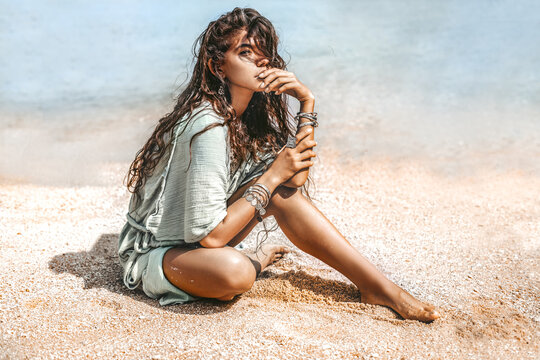 Beautiful young stylish woman sitting on sand on the beach