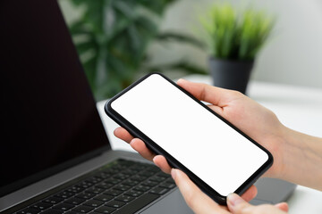 Woman hand holding smartphone with blank copy space screen for your advertisement. laptop on the table.