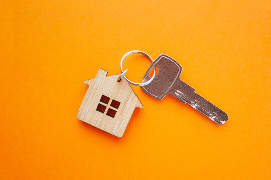 Key and house shaped keychain arrangement on orange background. Top view, flat lay. Real estate, insurance concept, mortgage, buy sell house, realtor concept.