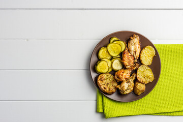 baked potatoes and chicken on a brown plate with pickled cucumbers