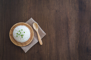 Cooked white rice in a wooden dish with green onion sliced on top with wooden spoon, and placemat on a wooden table. Thai Jasmine rice.