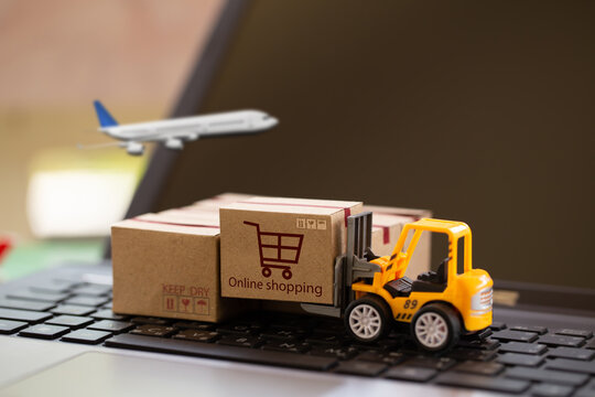 Logistic and cargo freight concept: Fork-lift a truck moves a paper box on notebook keyboard. depicts International freight or shipping service for online shopping.