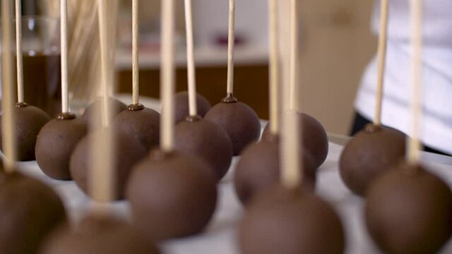 Woman putting wooden stick in little chocholate ball to make cakepops. In back line of assortment.