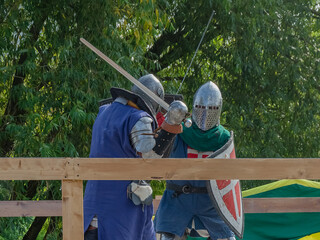 Two foot warriors in heavy medieval armor fight in the arena. Armed with swords. They are protected...